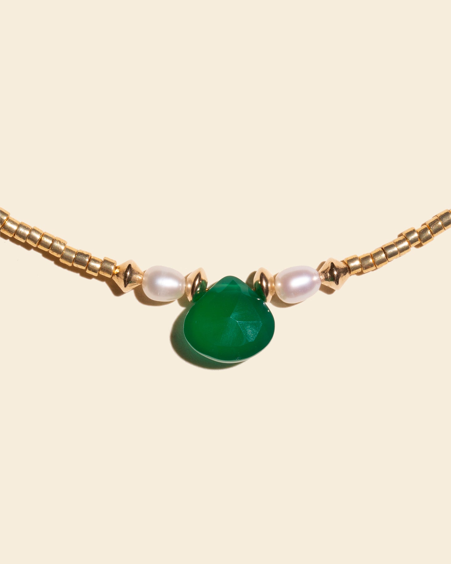 Gros plan sur les perles nacrées et la pierre d'onyx verte du bracelet de cheville Euphoria. Détails du bijou Apsara.