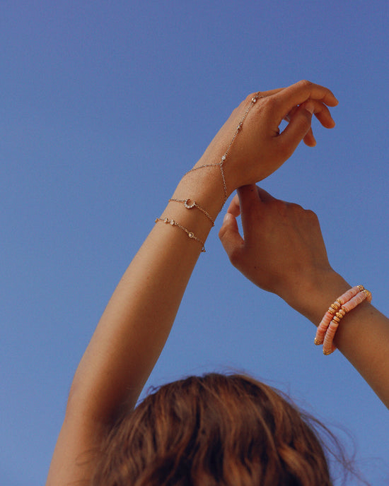 Composition de bijoux APSARA avec le bracelet Selene et une chaîne de main, sur fond de ciel bleu. Bijoux de créateur en plaqué or, faits main en France.