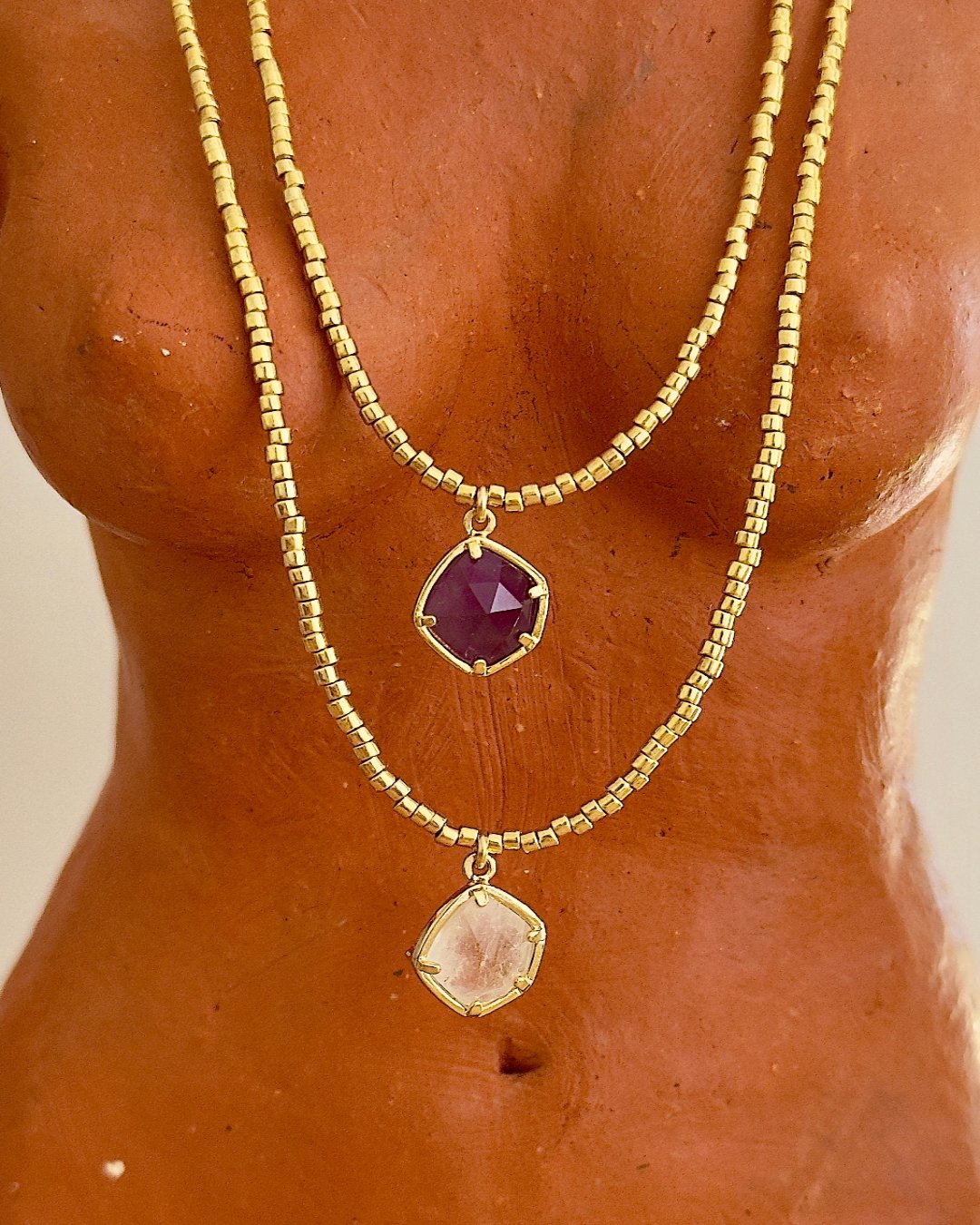 APSARA -  Accumulation de colliers ras-de-cou AMETHYST en améthyste et CRISTAL CLEAR en cristal de roche sur un buste de femme sculpté.