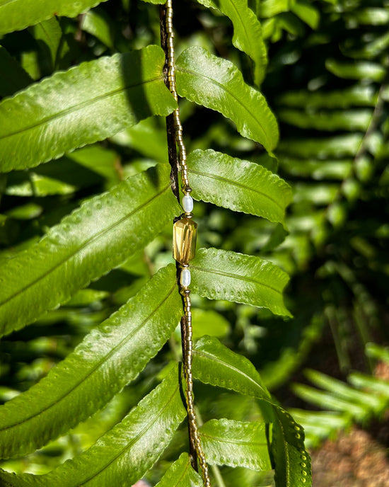 APSARA - Collier ras de cou COCO en orné d'une pépite de citrine et de perles dorées, présenté sur une feuille exotique.