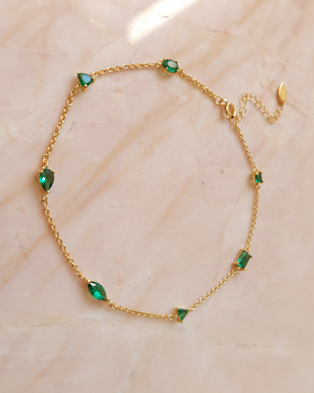 Bijou de pied Seven Emerald avec 7 zircons de différentes formes, vu de dessus sur fond rose. Bijou de créateur Apsara.