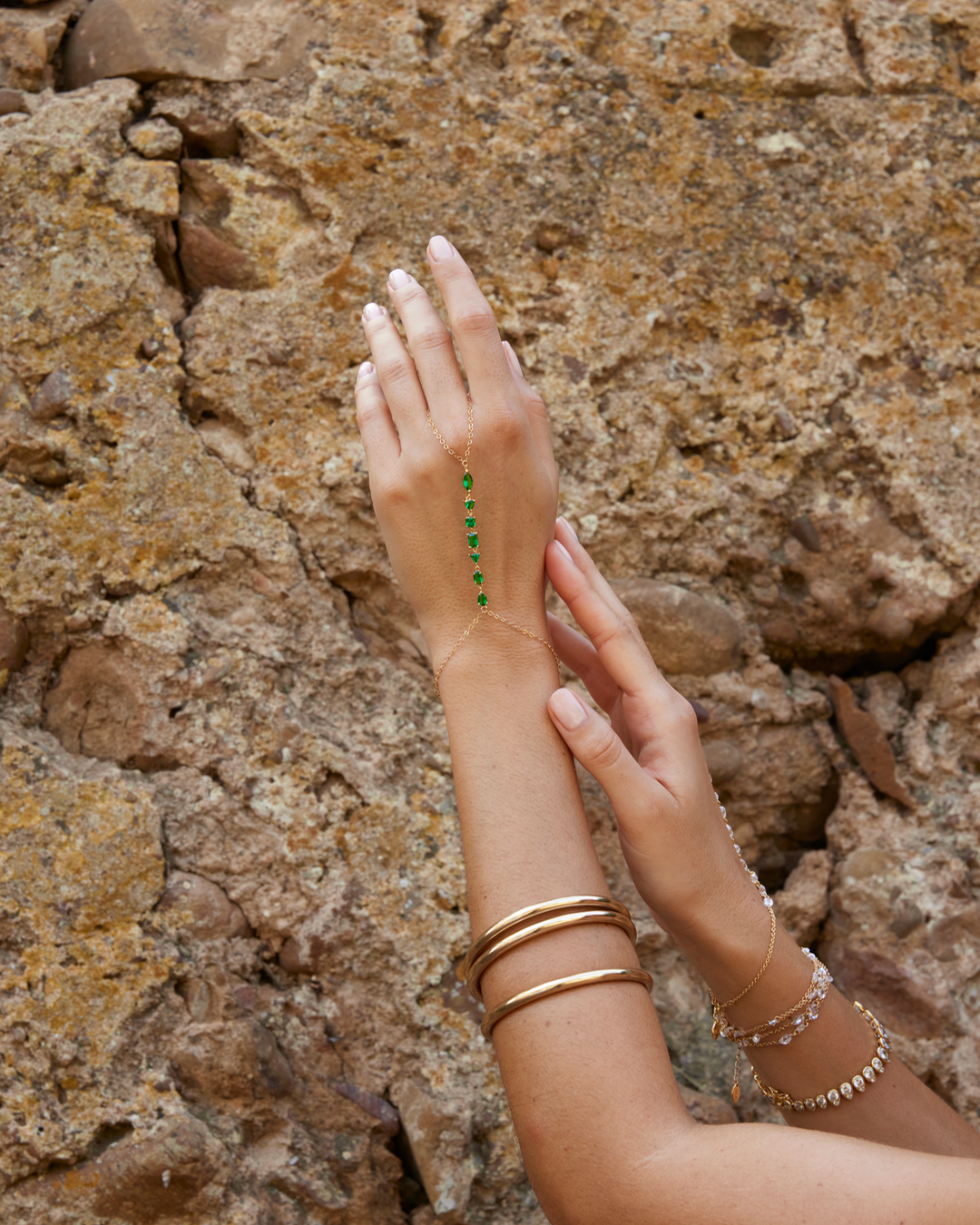 Chaîne de main Seven Emerald portée en accumulation avec d'autres bracelets dorés.