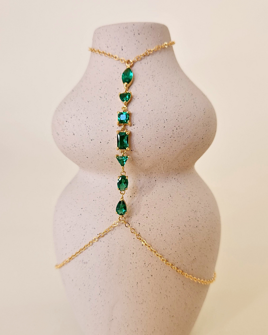 Chaîne de main Seven Emerald, fine chaîne en plaqué or avec 7 cristaux zircons vert émeraude de formes différentes, posée sur un vase. Bijou de créateur Apsara.