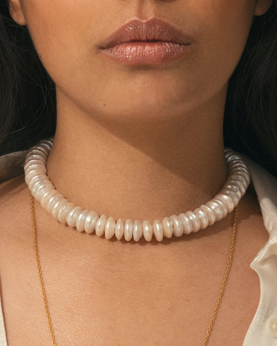 Gros plan sur le collier Holika APSARA et ses larges perles rondelles de nacre, porté sur le décolleté d'une femme.